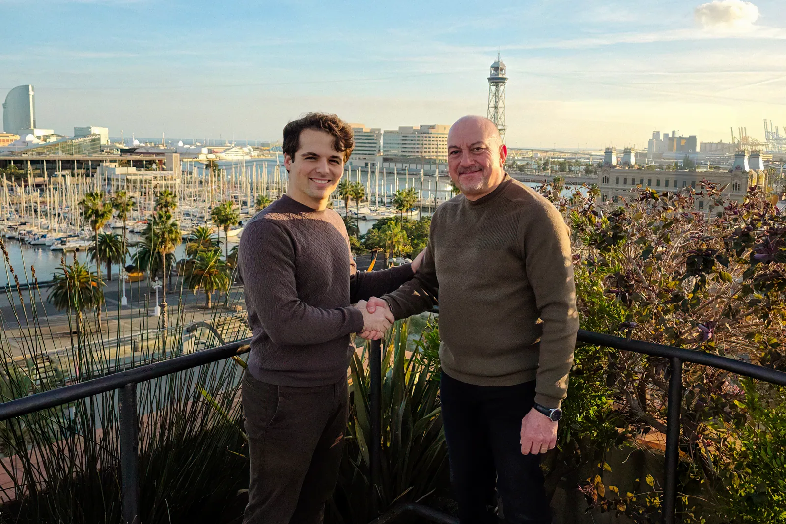 Arnau Salvadó of Atelier Cala and Juan Ignacio Martinez of Southern Ocean Marine Engineering shaking hands, with Barcelona's Port Vell in the background
